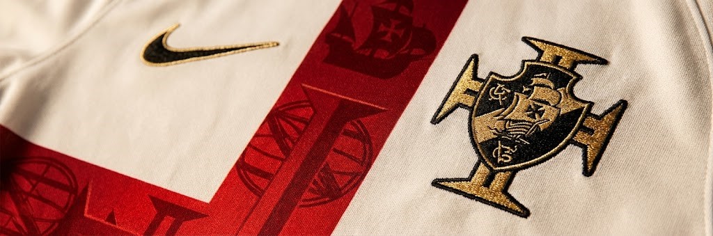 Close-up mostrando a textura de caravelas e a Cruz da Ordem de Cristo na camisa off-white do Vasco